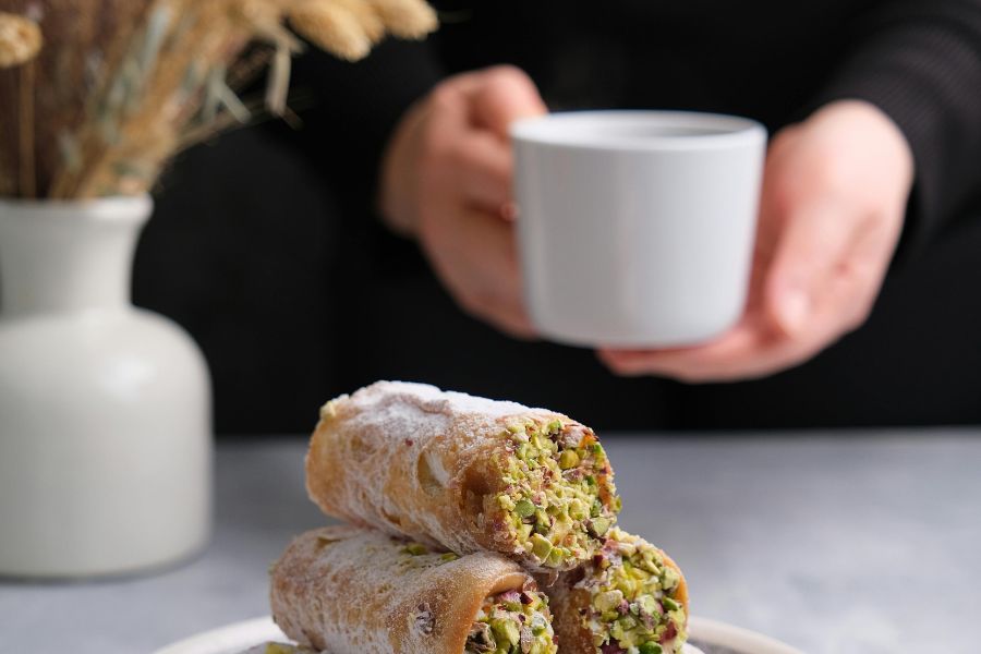 persona cogiendo taza de café y cannolis rellenos en un plato