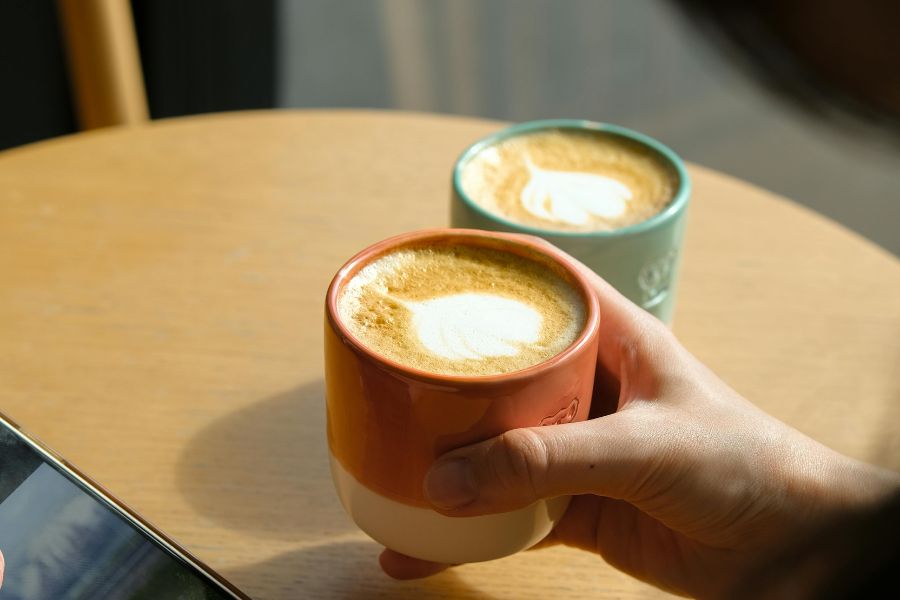 chica cogiendo taza de café y otra taza de café al lado